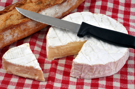 Camembert entamé sur une nappe à carreaux avec du pain et un couteau