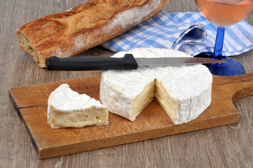 Camembert posé sur une planche à découper avec du pain et un verre de rosé