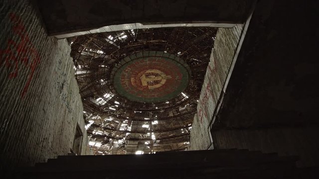 Camera tracks to the entrance of the main auditorium at the ruined Buzludzha monument in Bulgaria, showing the Soviet hammer and sickle