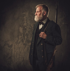 Senior hunter with a shotgun in a traditional shooting clothing, posing on a dark background