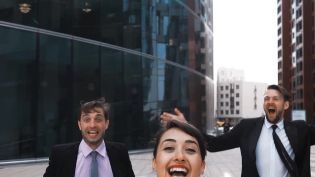 Slow motion. 3 attractive positive happy exulting of lucky win Businesspeople jump high in air with smiling wite teeth. Glass contemporary building dackground. Middle Rapid shoot. Sunrise.