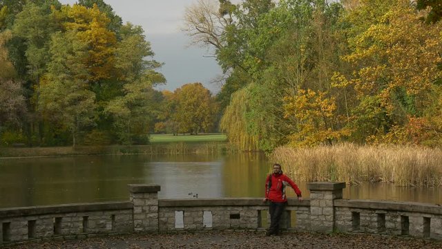 Tourist Resting in Park Standing on a Bridge Cloudy Day Autumn Sunlight View From Observation Deck Landscape Yellow Trees Dry Reed Ducks Are Swimming