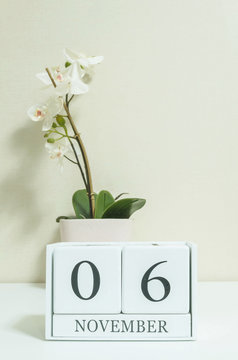 Closeup white wooden calendar with black 6 november word with white orchid flower on white wood desk and cream color wallpaper in room textured background , selective focus at the calendar