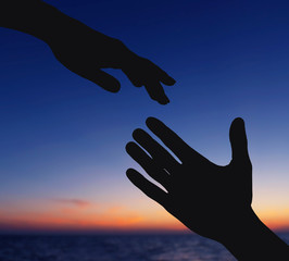 Silhouettes of female and male hands reaching to each other on sky background. Help and care concept.