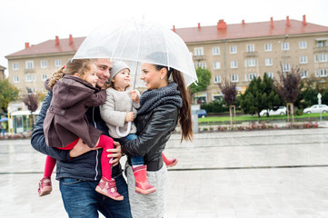 Young family with two daughters under the umbrella, town