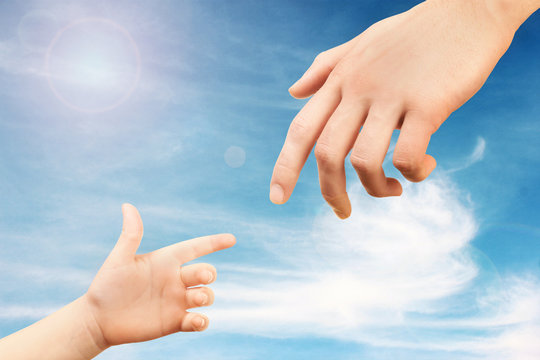 Father and child hands reaching to each other on sky background. Help and care concept.
