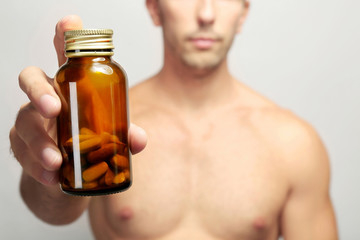 Muscular man holding drugs in bottle, closeup