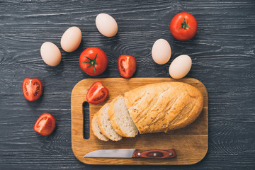 Food background, ingredients on black wooden table. Fresh tomatoes and eggs, homemade sliced bread and a knife. Healthy food, cooking concept.