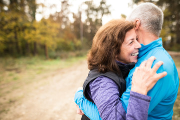 Beautiful senior couple running outside in sunny autumn forest