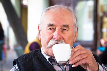 Elderly man with cup of coffee at summer cafe