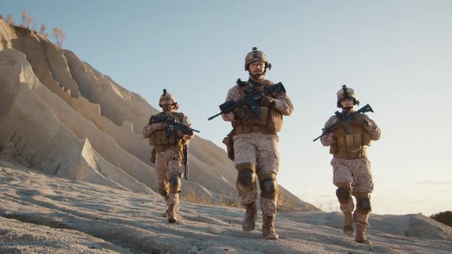 Squad of Three Fully Equipped and Armed Soldiers Walking in Desert Environment. Slow Motion.