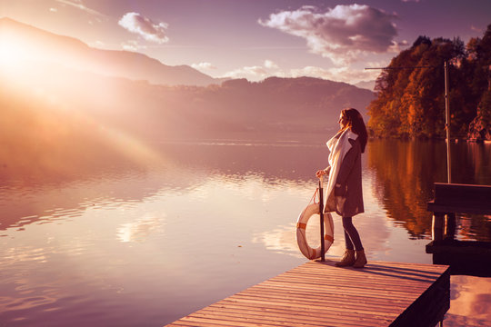 woman standing on a bridge by the lake in sunset