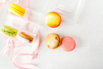 Open a transparent gift box with cakes macarons on a white wooden table. Top view, copy space