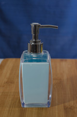 Obraz premium Light blue liquid soap dispenser with a chrome top on a wooden shelf with a dark blue background