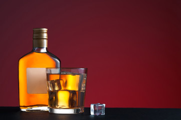Whiskey on the rocks and glass bottle in red background