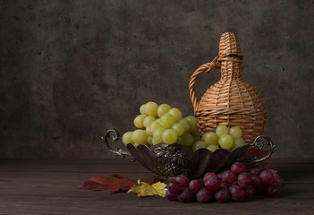 green grapes in a vase on a background of a bottle on a wooden table