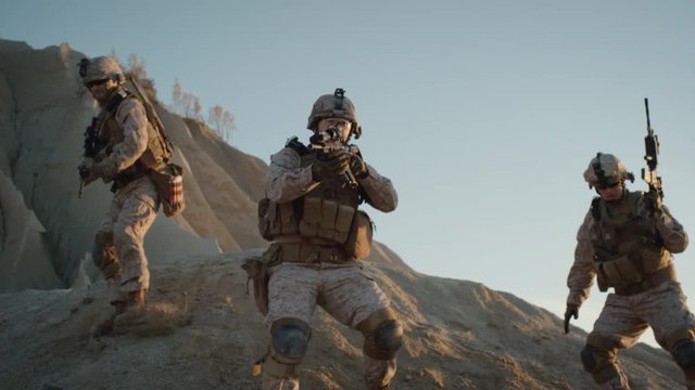 Squad of Three Fully Equipped and Armed Soldiers Standing on Hill in Desert Environment in Sunset Light. Slow Motion.