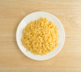 Shoepeg white corn with a butter sauce on a dish atop a wood table.