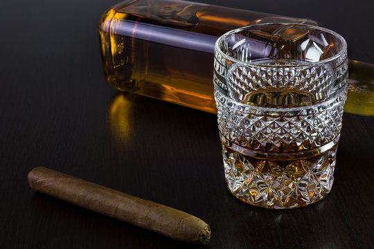 A glass of whisky, a bottle and a cigar on black.