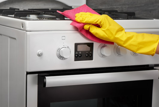 Hand in yellow glove cleaning white stove with pink rag