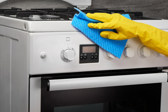 Hand in yellow glove cleaning white stove with blue rag