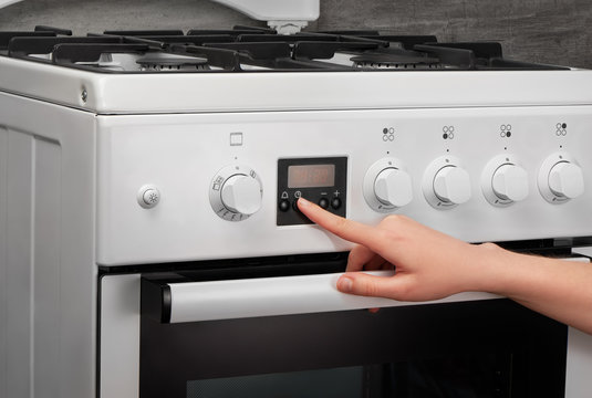 Female hand turning on white kitchen gas stove on gray