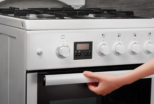 Female hand opening oven in white kitchen stove on gray