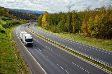 Asphalt highway with oncoming white trucks in the autumn landscape.