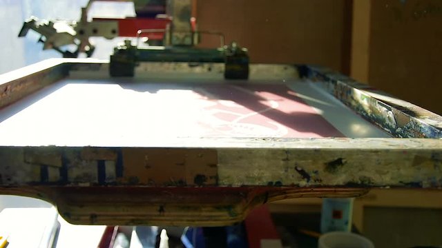 Traditional silk-screen printing preparation - artist inserts blank paper and places black ink on top of the screen