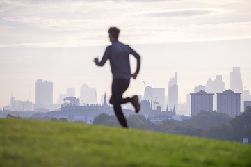 Abstract silhouette of jogger running on the green grass of Primrose Hill in front of the misty London city skyline