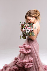 Beautiful woman in a pink dress posing with a bouquet.