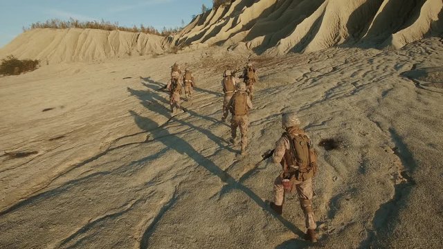 Flying over Group of Running Soldiers in Desert Environment.