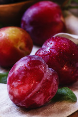 Red plums with leaves, wood background, selective focus