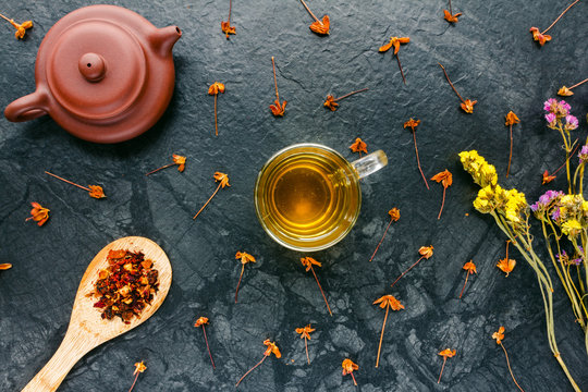 Herbal tea in glass, dried tea in wood spoons, teapot on black background