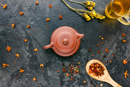 Top view of brown teapot, dried herbs and flowers on black background