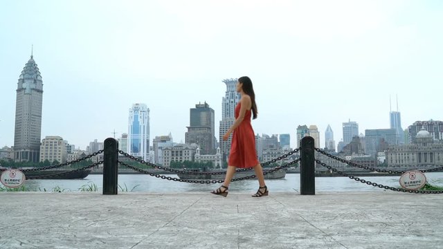 Shanghai woman walking in Pudong by huangpu river with view of the Bund. Tourist or casual girl in beautiful red dress enjoying walk at Pudong boardwalk.