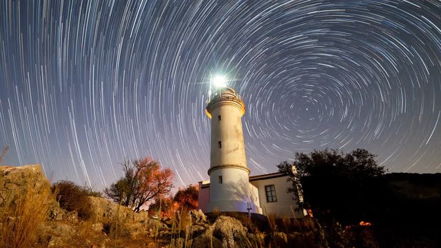 Timelapse of beautiful night landscape with lighthouse with rotating starry sky on a background