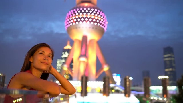 Shanghai woman or tourist thoughtful looking at city lights at night by Oriental Pearl Tower in Pudong, China. Multicultural Asian Chinese / Caucasian young woman professional in financial district.