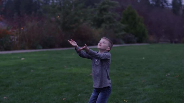 Father and son passing a football in a park at night, slow motion