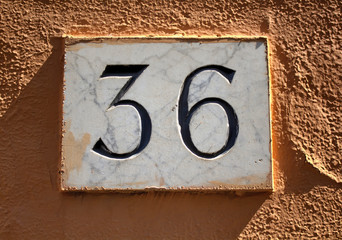 Engraved building number (36) made with marble on plastered wall in Rome.