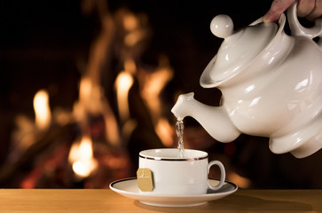 Water being poured into a cup of tea with a fireplace on the background