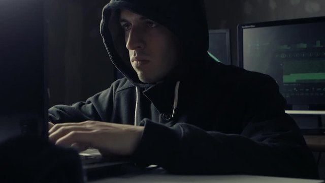 hacker in a hooded working on a computer in a dark office room