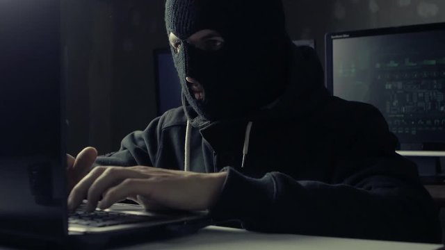 Dangerous hacker in a mask working on a computer in a dark office room