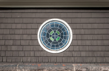 Decorative stained glass round window. Isolated stained glass circle window, Wood shingle siding with round window frame. Abstract art and design. Abstract colors and design. Architecture design. 