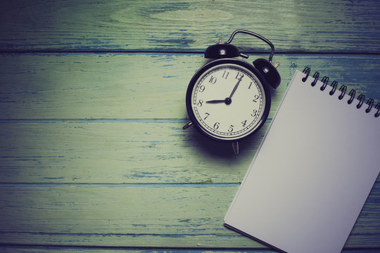 notebook with retro clock on wooden table, top view image, retro