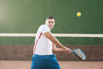 Handsome young man on tennis court. Man playing tennis. Man hitting tennis ball