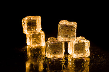 Ice cubes of gold color on a reflective surface.