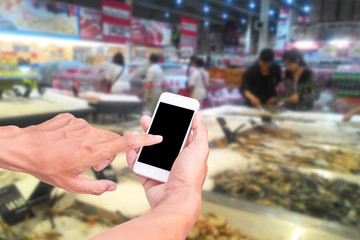 Male hand holding mobile smart phone on Supermarket blur backgro