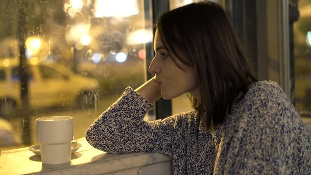 Pensive woman looking out of window sitting in cafe at night
