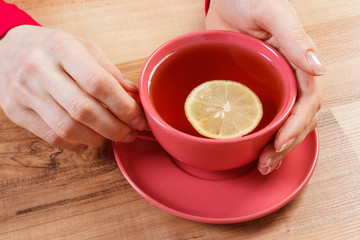 Hand of woman holding cup of hot tea on table